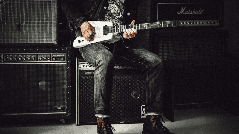 Guitarist playing electric guitar in a music studio with amplifiers and sound equipment, illustrating music production, live performance, and audio engineering.