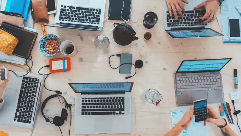 Laptops, smartphones, and digital devices on a wooden desk in a collaborative workspace for music industry professionals and