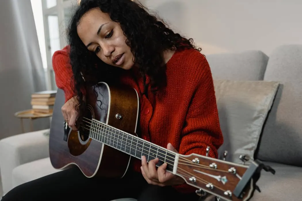Guitarist woman playing acoustic guitar in cozy home setting, enjoying music practice, casual and relaxed atmosphere, indoor