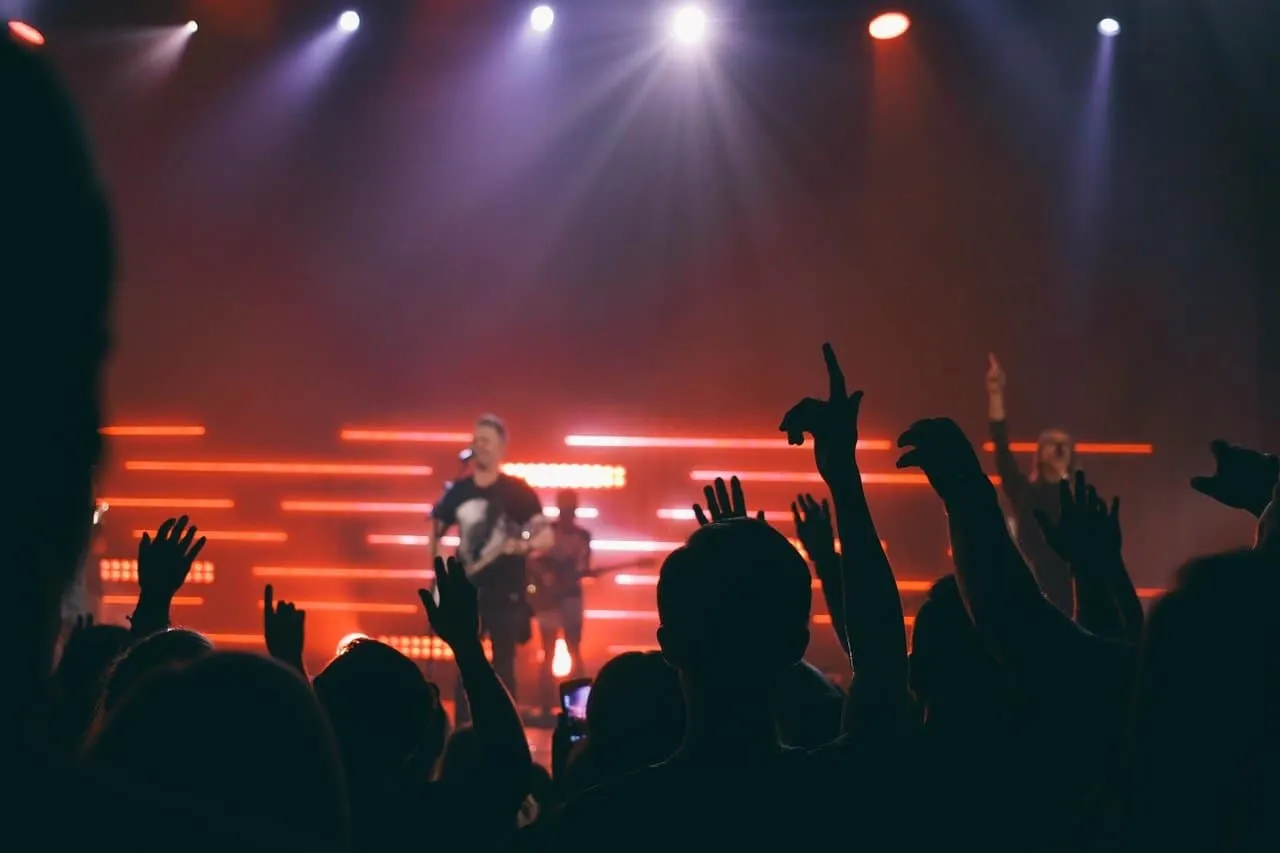 Concert crowd cheering with hands raised at music festival, stage lighting, live music performance, entertainment event, audi