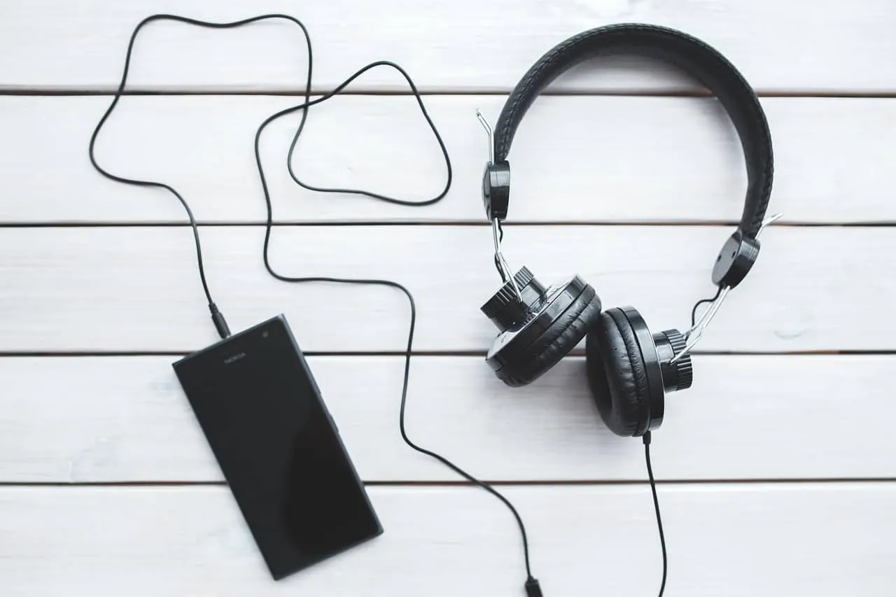 Headphones with connected smartphone on white wooden surface, music streaming technology, audio device, podcast, music listen