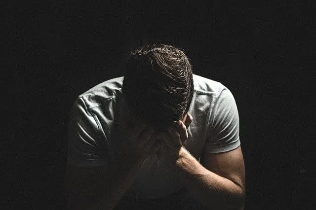 Deep thinking man holding head in dark room, mental health support, stress management, emotional struggle, personal well-bein